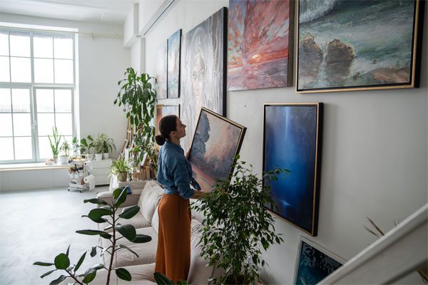 Image of woman hanging paintings on her wall